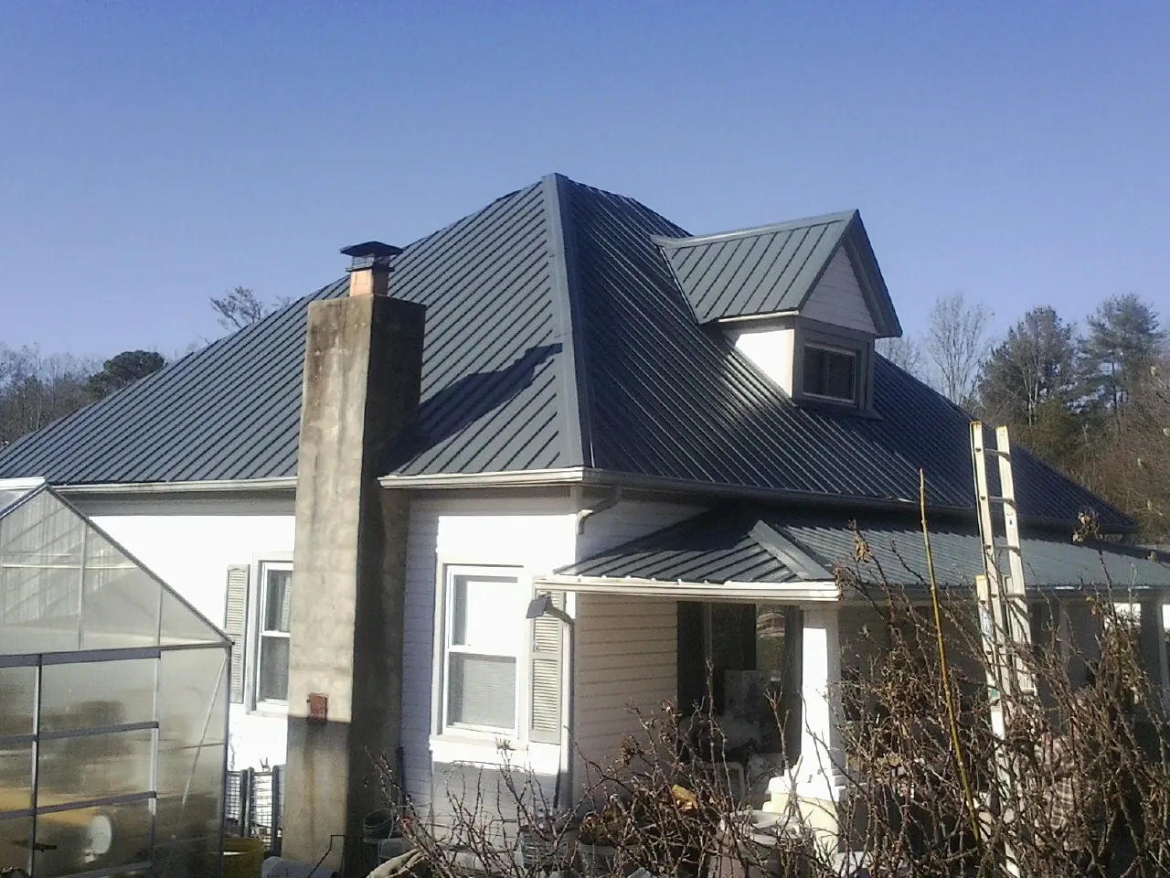 Dark blue standing seam metal roof on a white farmhouse with dormer — Slate & Tile Roof Repair by Roofing Brothers in Platteville