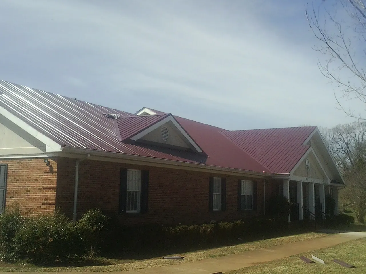 Red metal roof with gabled entries on a long brick building, from a Hail Damage Roof Repair job in Platteville