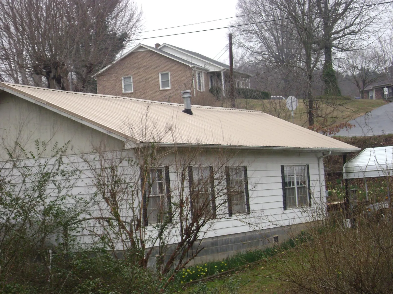 Tan metal roof on a white sided house set into a hillside — Commercial Roofing by Roofing Brothers in Platteville